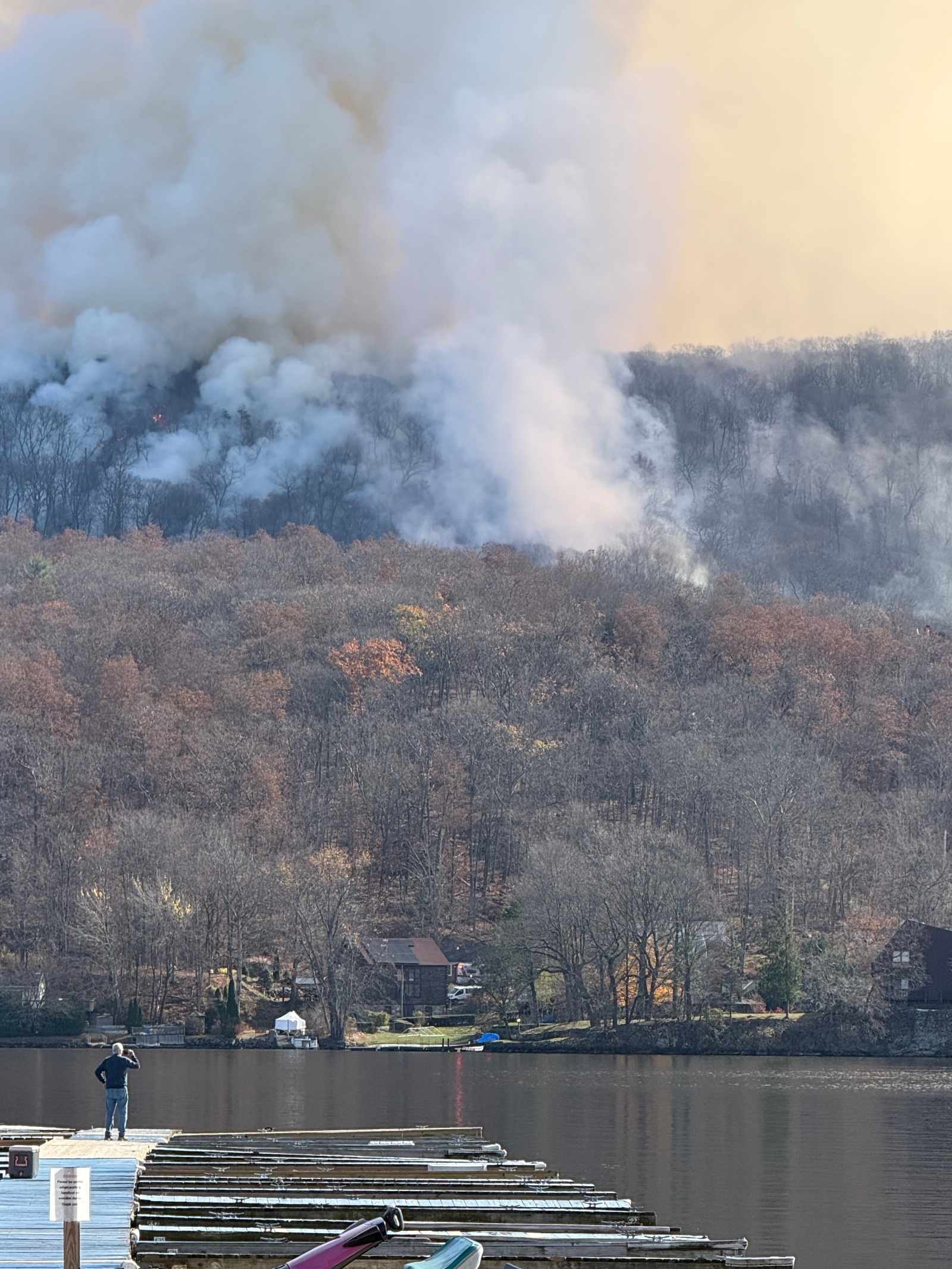 White smoke billows from an autumn forest on a lake