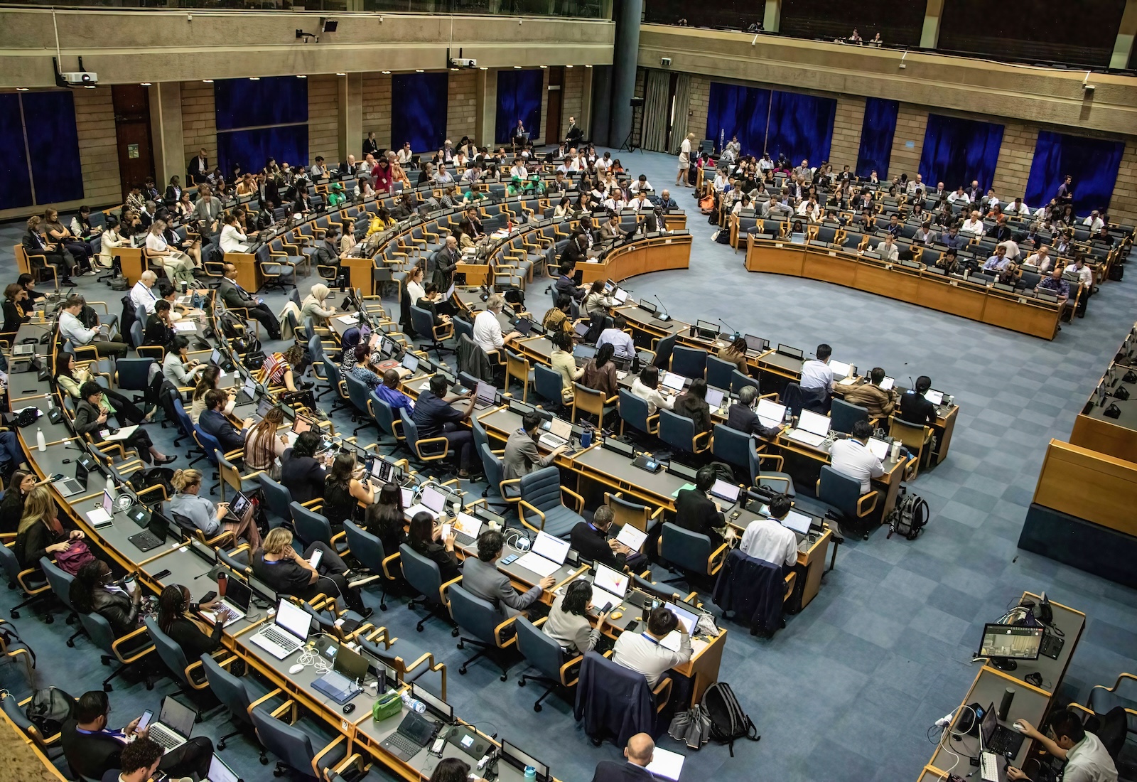 Aerial view of a large conference room, with people sitting at desks arranged in a large circle.