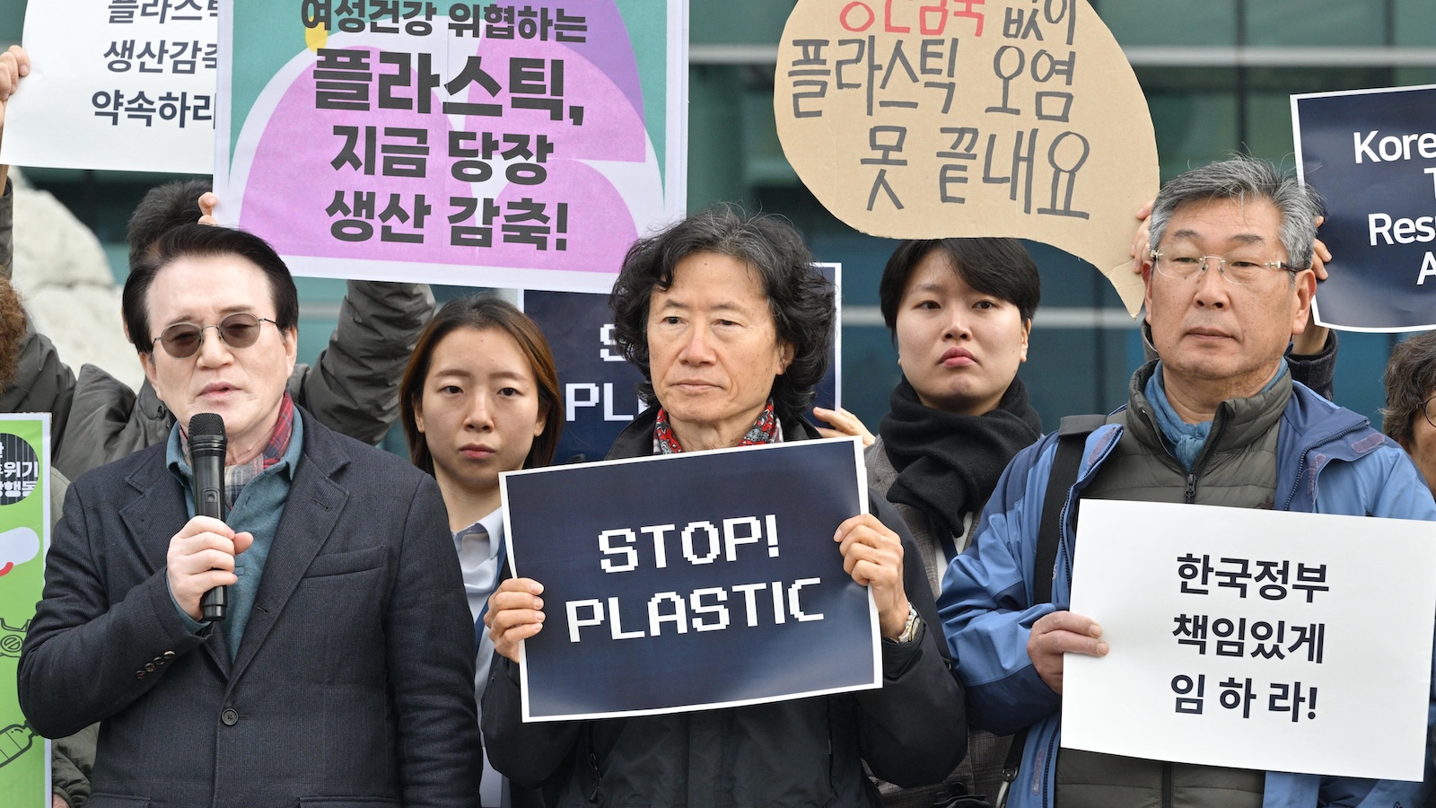 A small group of protesters hold signs, mostly in Korean, but one reads 