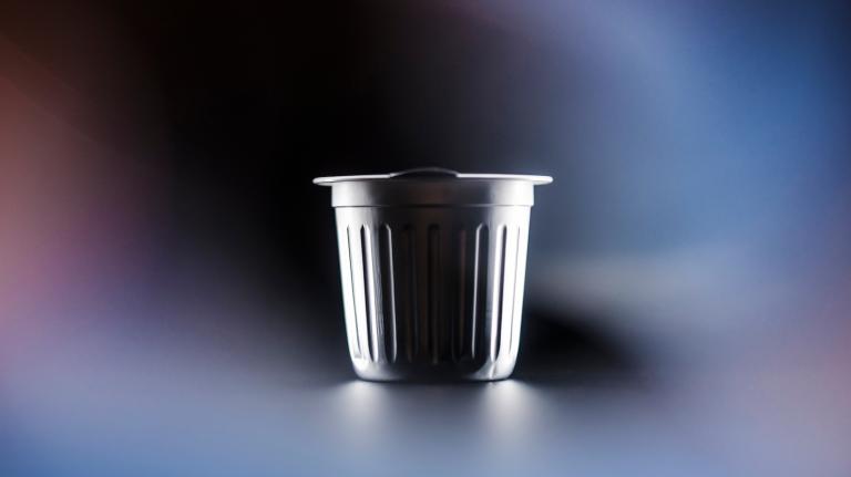 An aluminum single-serve coffee pod against a black and blue background