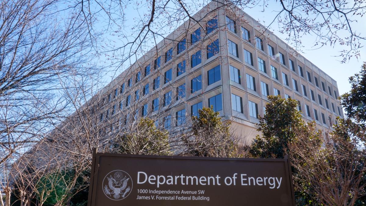 A large beige building with big dark grey windows looms over a department of energy sign