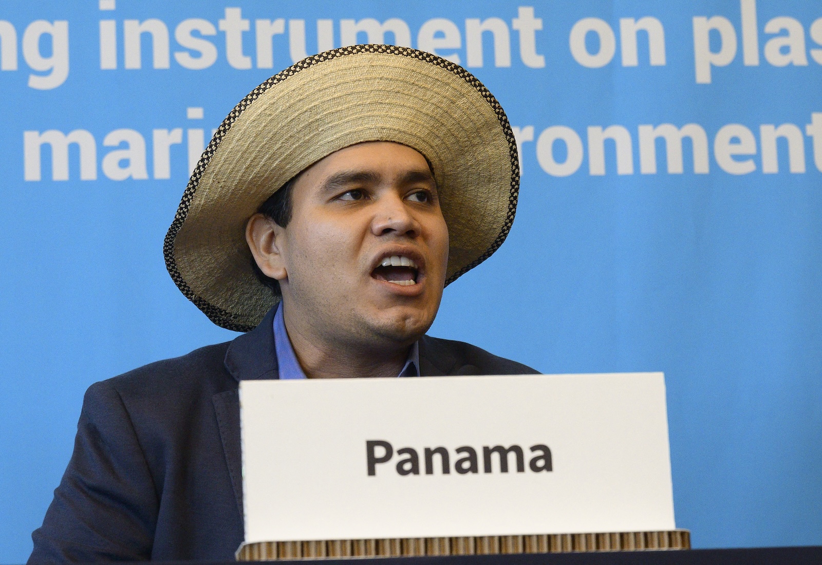 Juan Carlos Monterrey holding a placard "Panama" In front of him. He is wearing a wide-brimmed hat and is standing against a blue background.