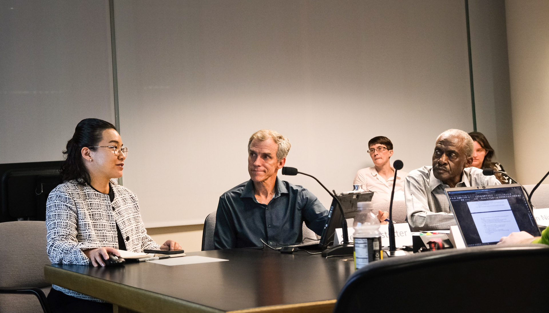 A group of people sits around a florescently-lit conference table. It is dark outside.