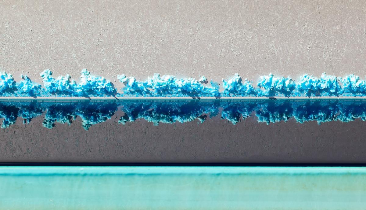 A horizontal line of bright blue crystals is reflected in liquid, underneath which is a teal line