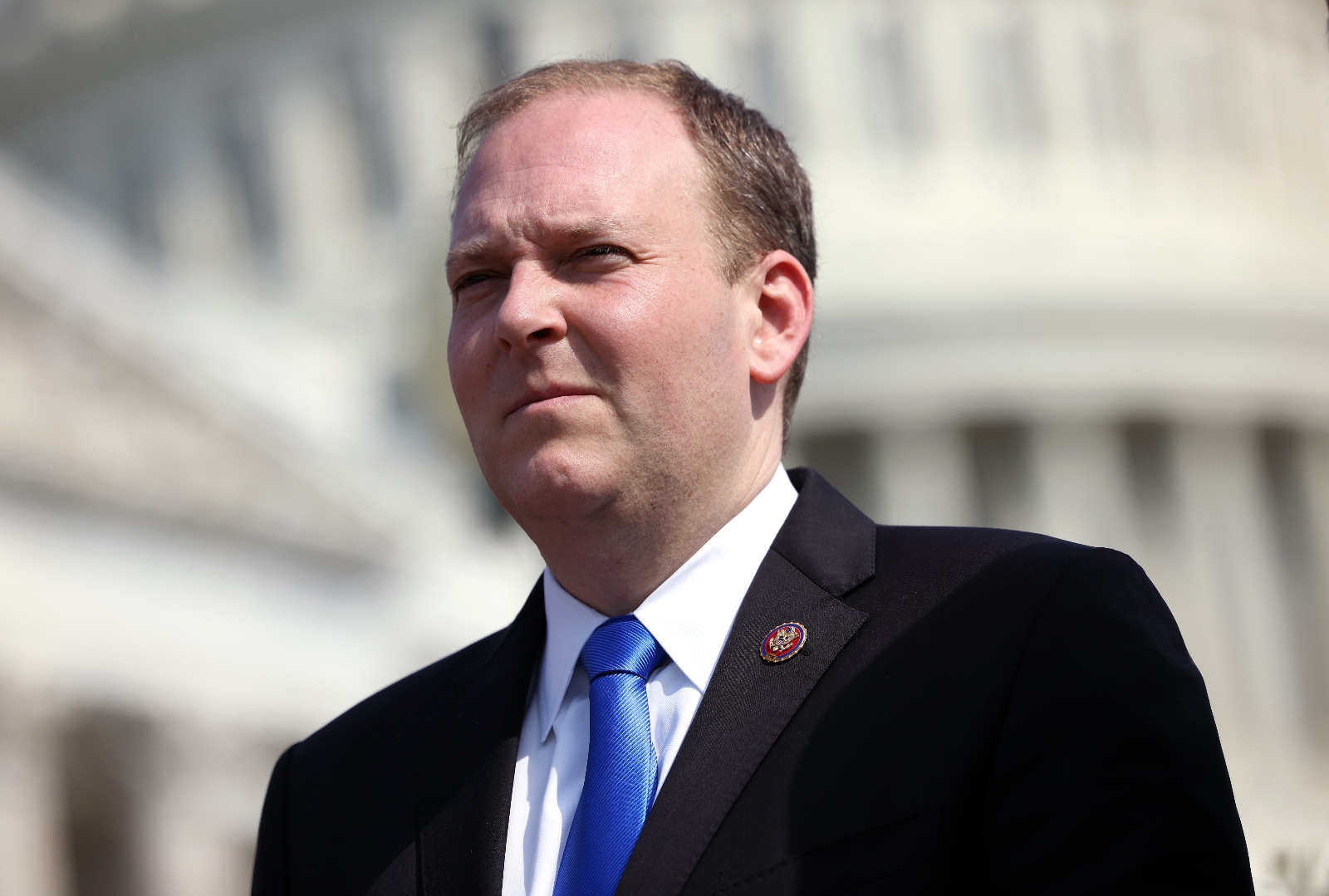 Closeup photo of a middle-age white man in a suit and blue tie, with Washington, D.C., buildings in the background