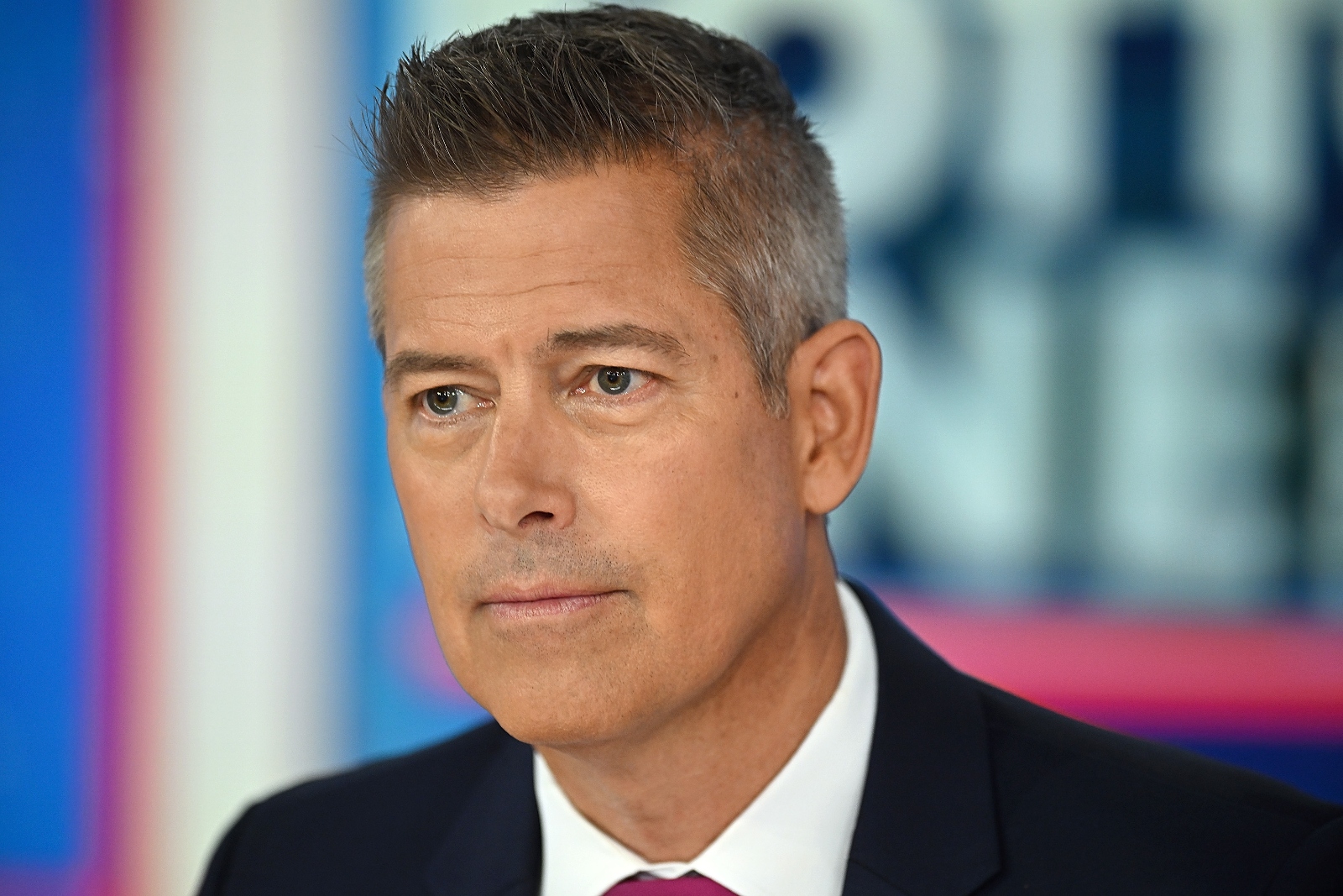 Close-up shot of a white man with graying hair wearing a suit and tie