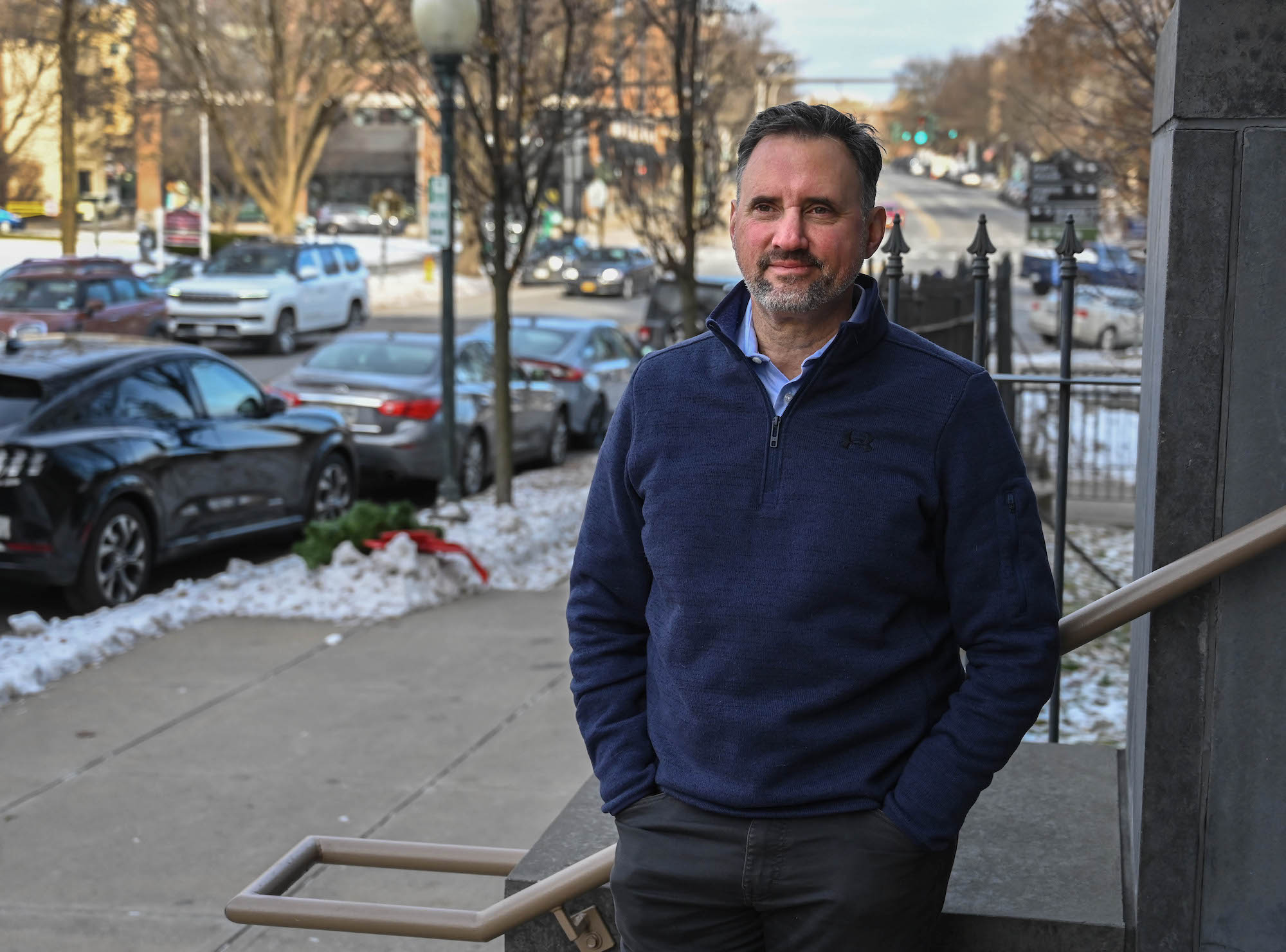 A man in a blue zip up sweater stands on a city street