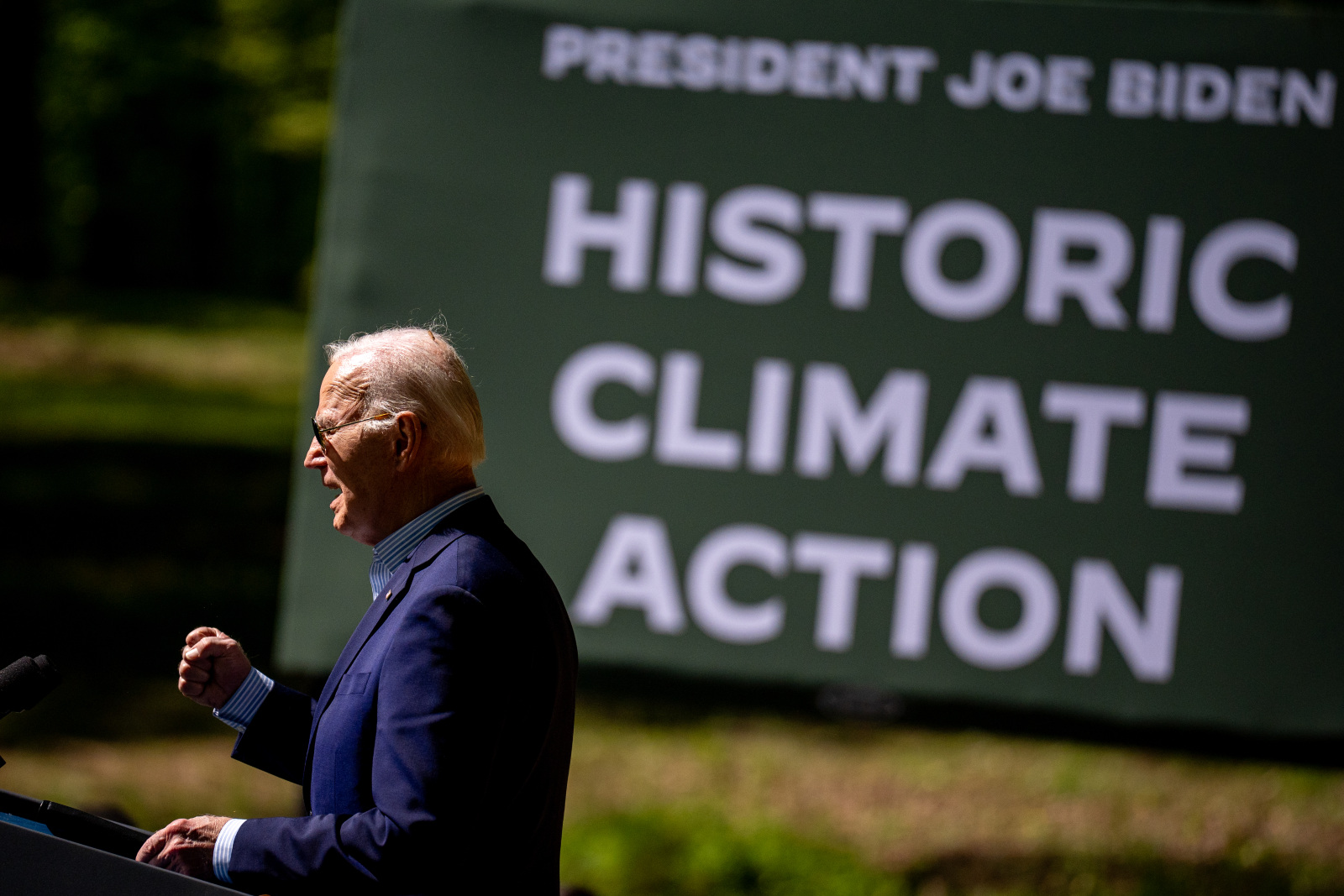 Photo of Biden giving a speech, taken from the side, with a sign saying "historic climate action"