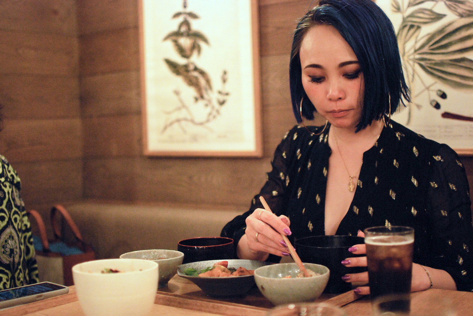 A woman uses chopsticks to pick food up from a bowl in a restaurant