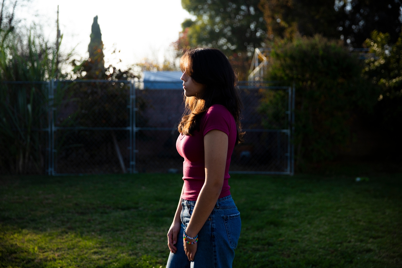 A girl in a red tee shirt and jeans walks on the grass in a yard