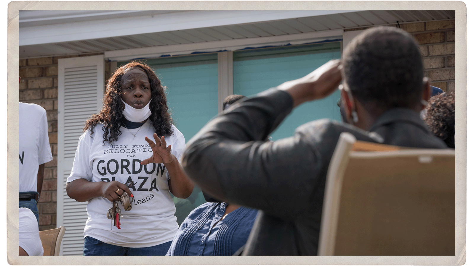 A woman in a shirt that says 'gordon plaza' talks to a man seated in a chair outside