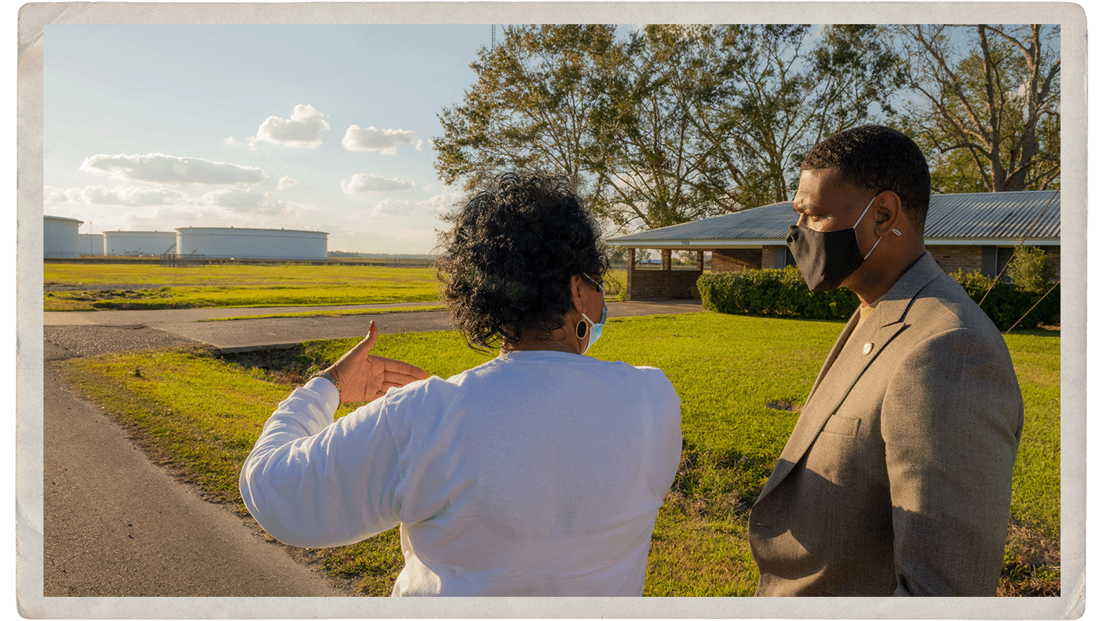 A woman and man stand facing a street leading toward an industrial plant.