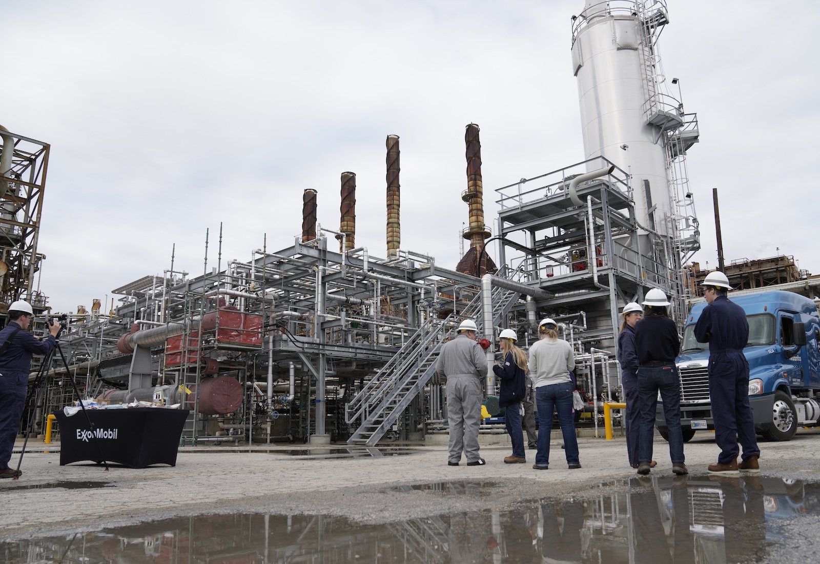 Workers stand in front of a large petrochemical complex with smokestacks