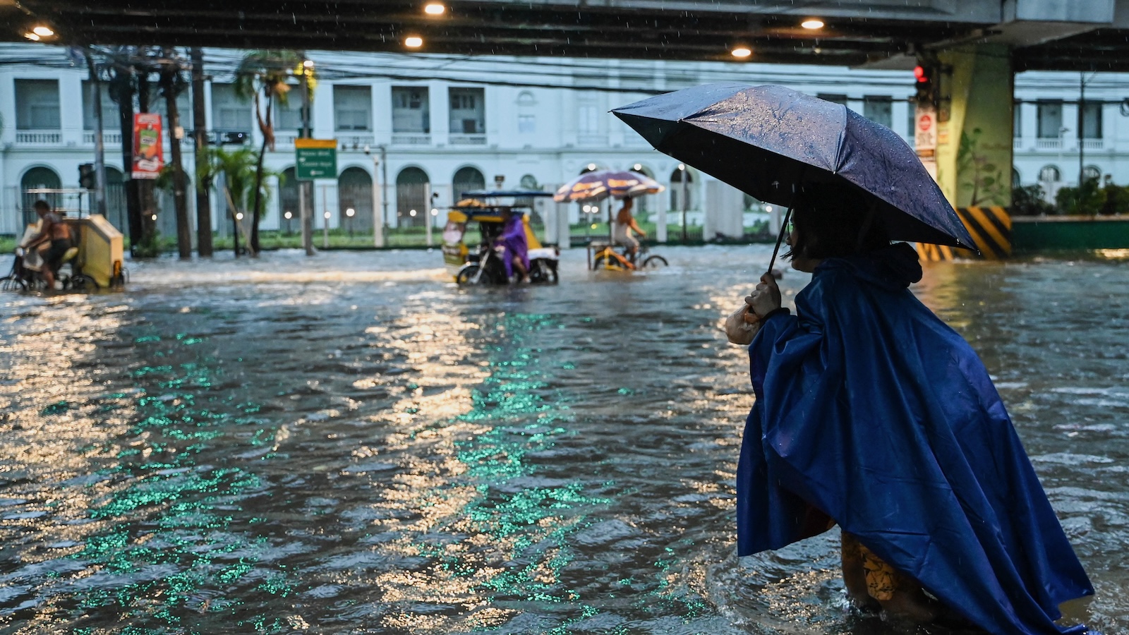 People walk along a flooded street in Manila on July 24, 2024 amid heavy rains brought by Typhoon Gaemi.