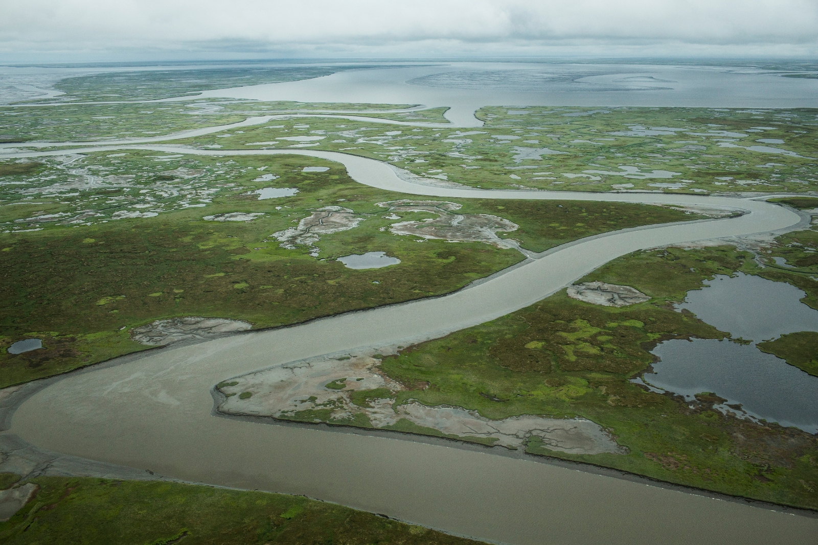 A river cuts through marshy green landscape with the sea beyond