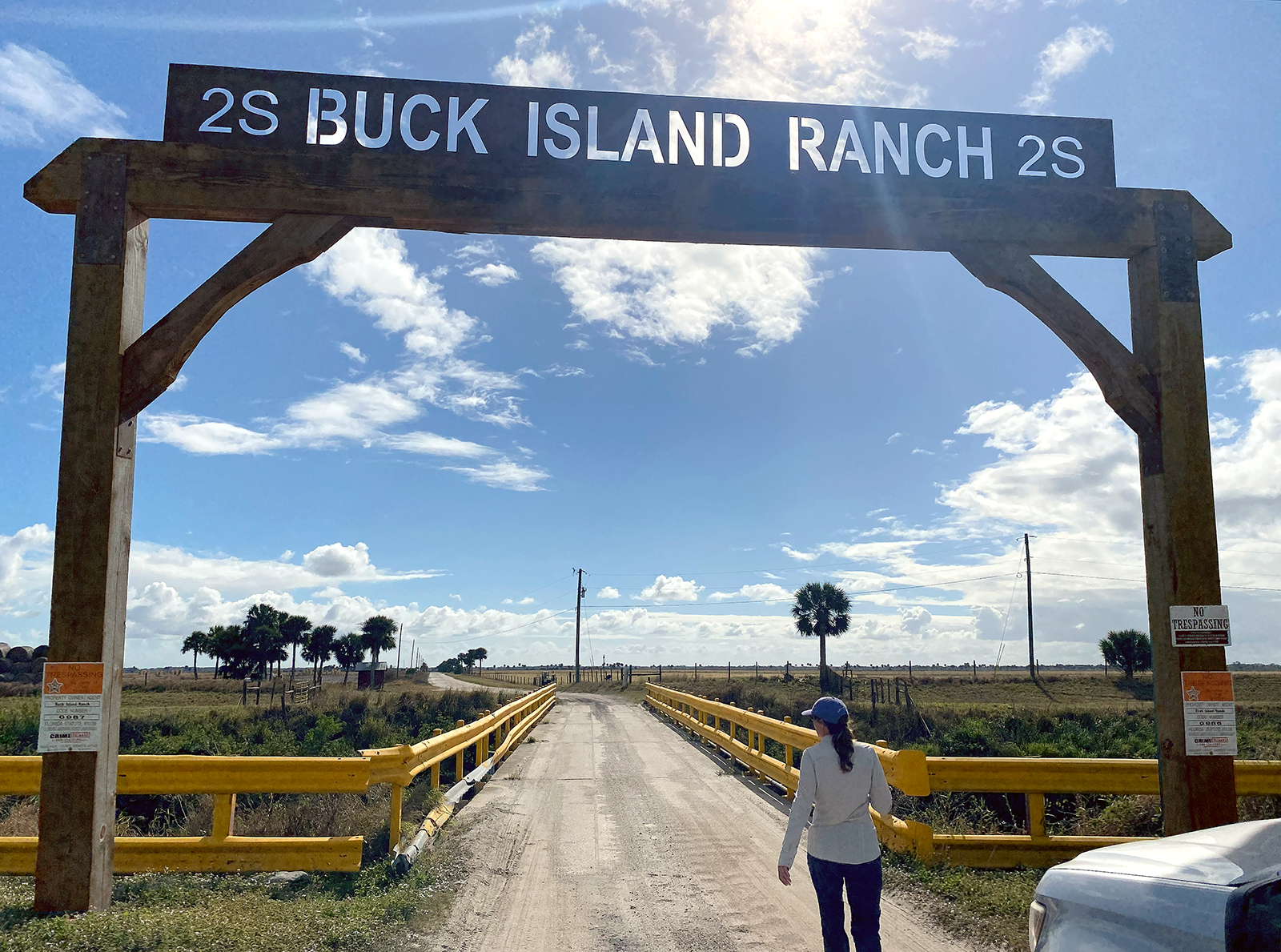 A woman in a hat walks under a ranch sign