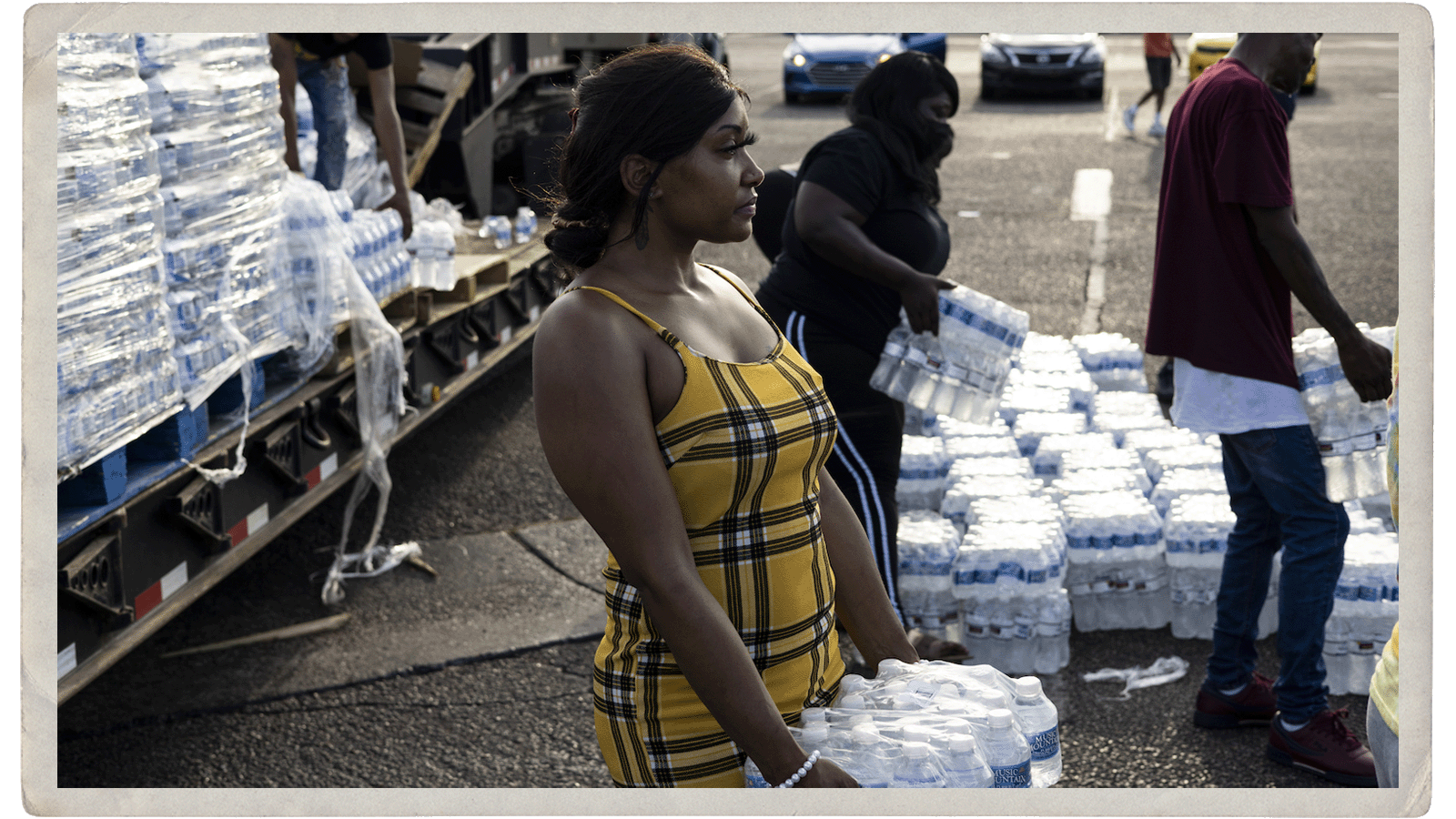 A woman in a plaid dress holds a pack of bottled water