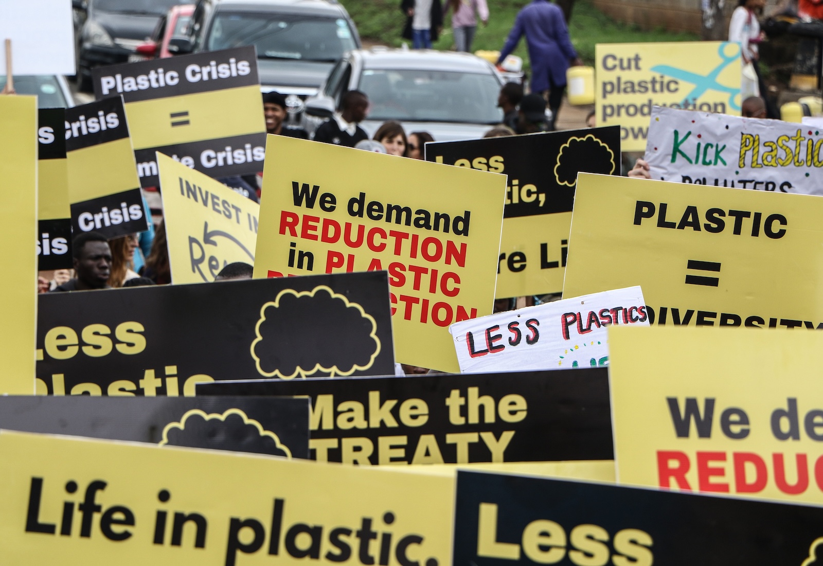 A number of yellow and black signs overlap, with messages calling for plastic reduction policies