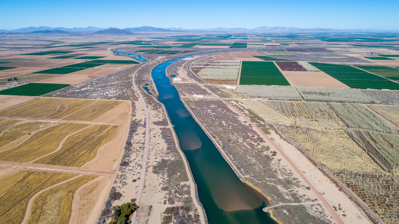 An overhead view of a blue green river cutting through a desert dotted with squares of green and brown farms