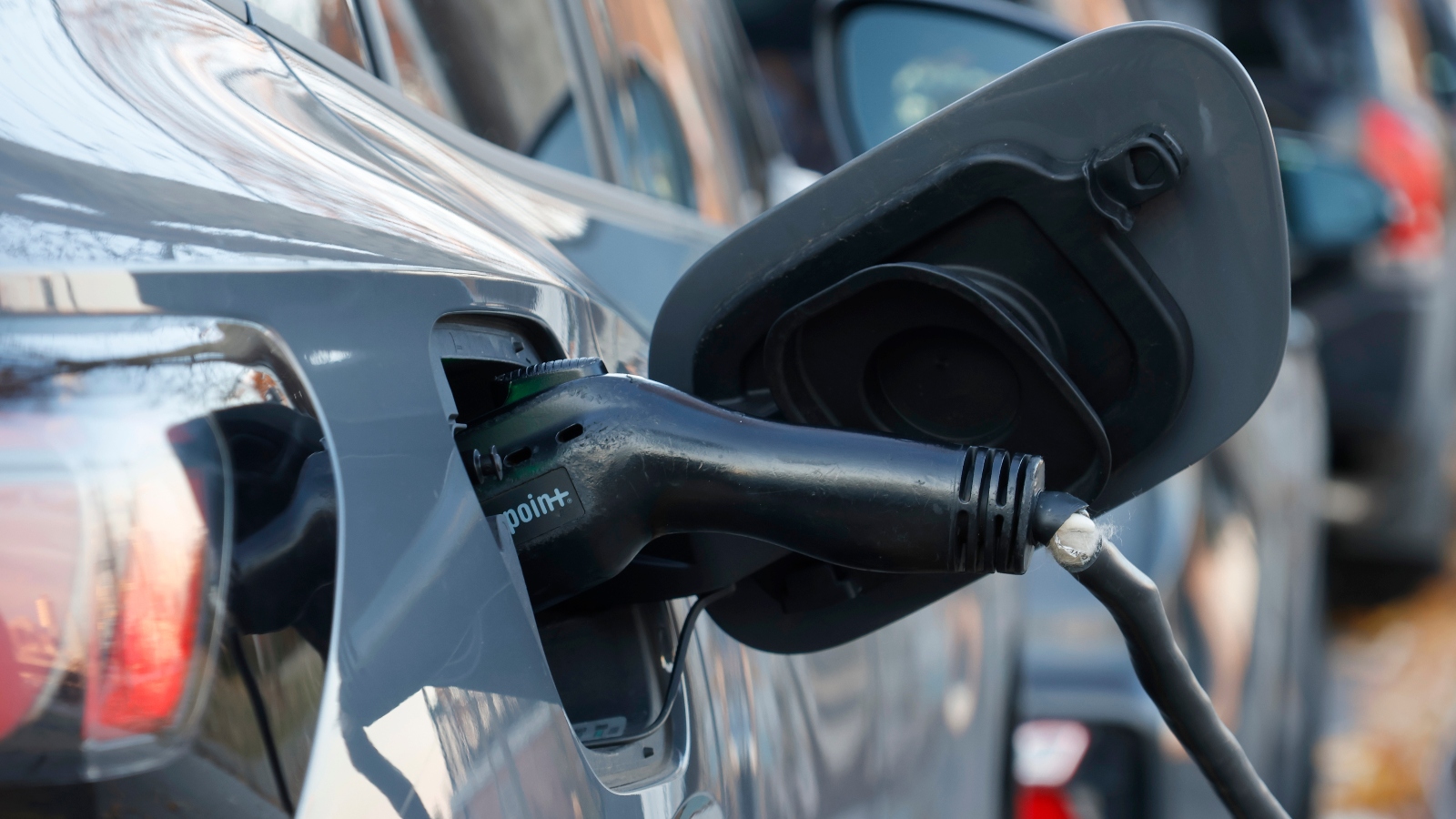 An electric charger is plugged into a gray car