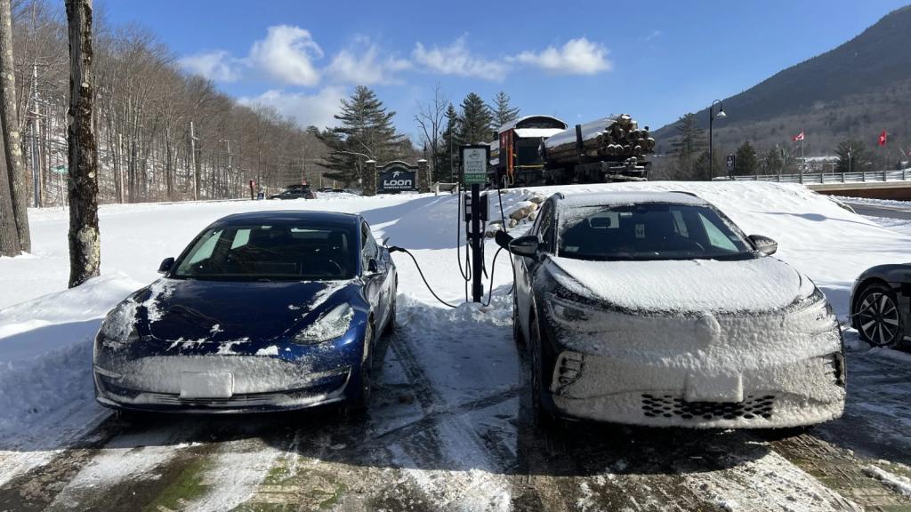Electric cars charge as they sit in the snow next to a forest