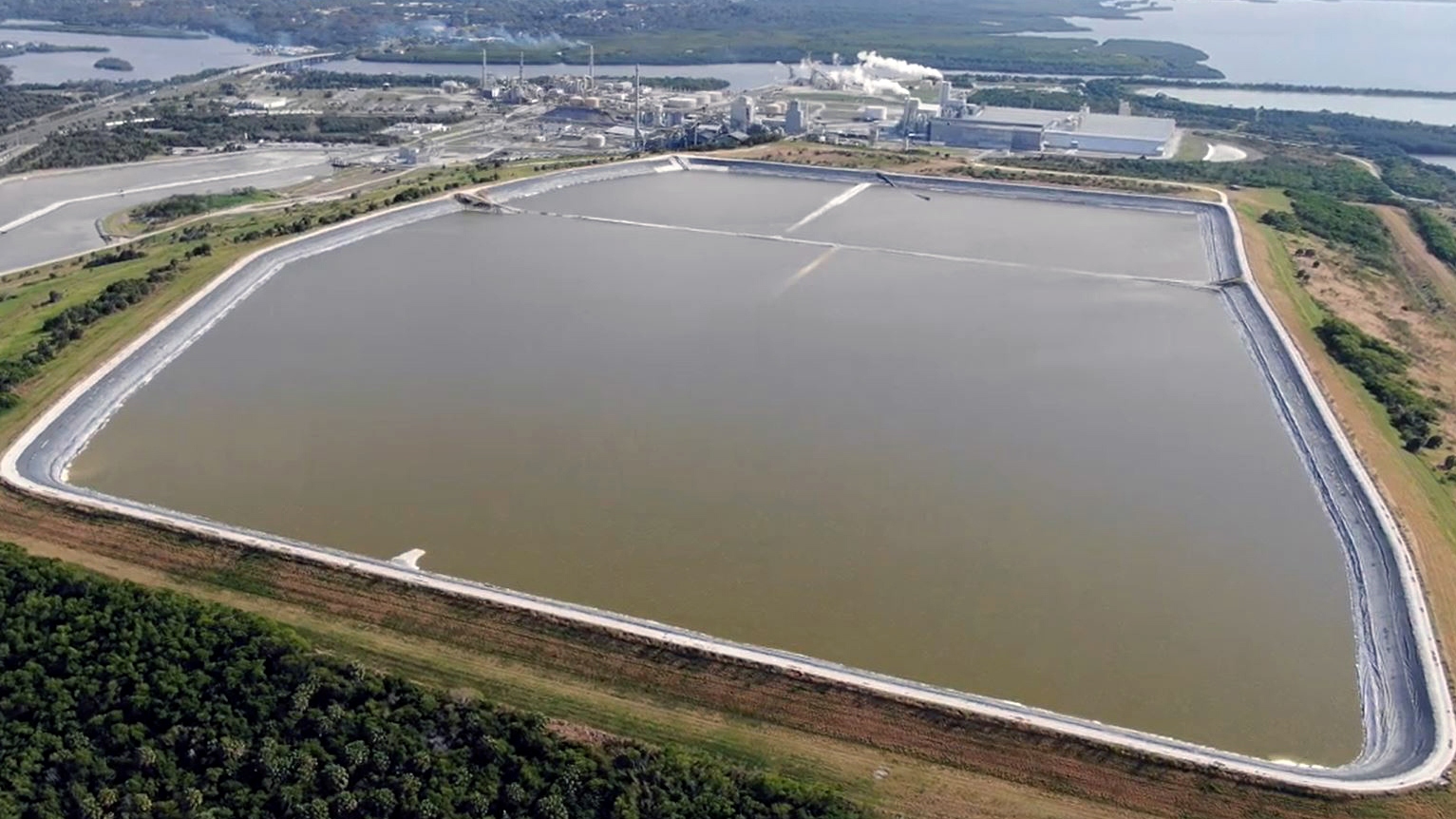 A large brownish green lake lies along the water in flat land