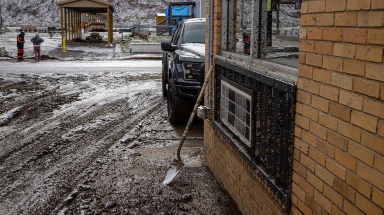 A shovel is seen leaning against a mud-splattered building with a parking lot awash in mud and water from the intense floods that hit eastern Kentucky in February, 2025.