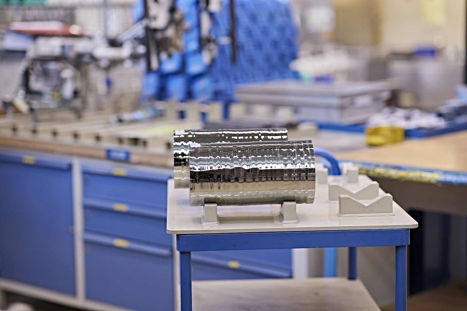 Two metallic cylinders sit on a blue and white table in front of laboratory equipment