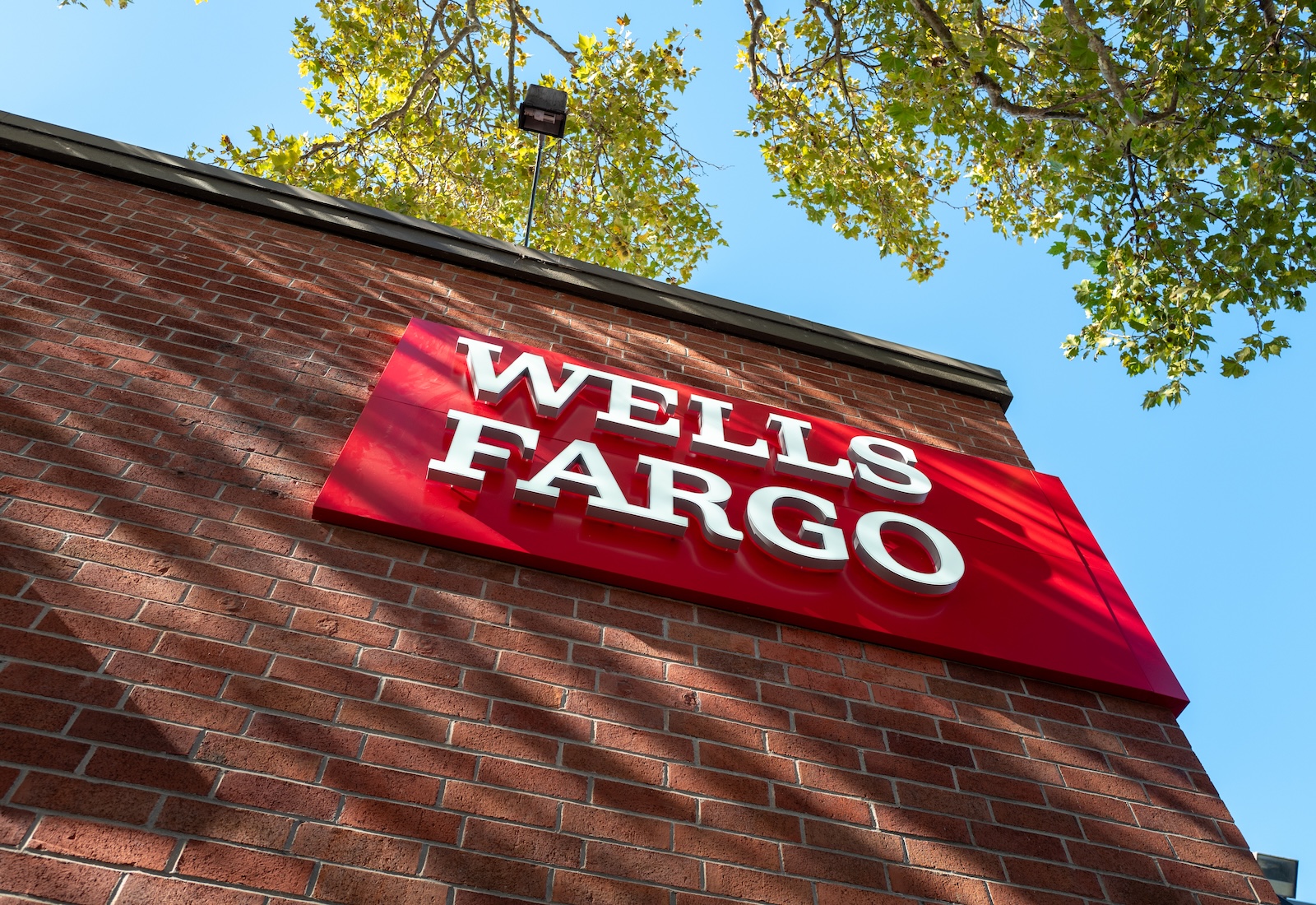 Exterior of a brick building with the Wells Fargo logo visible. Tree branches brush the building.