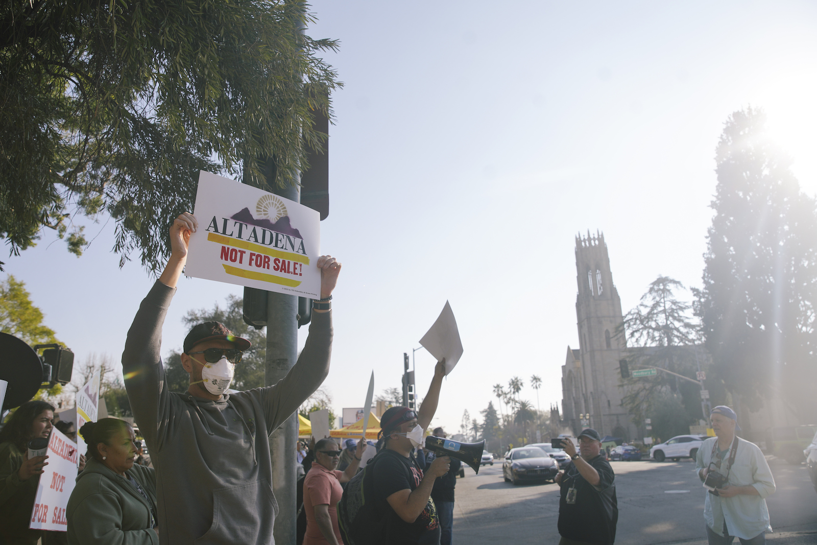 A group of people walk through the streets holding signs that say 'altadena not for sale'