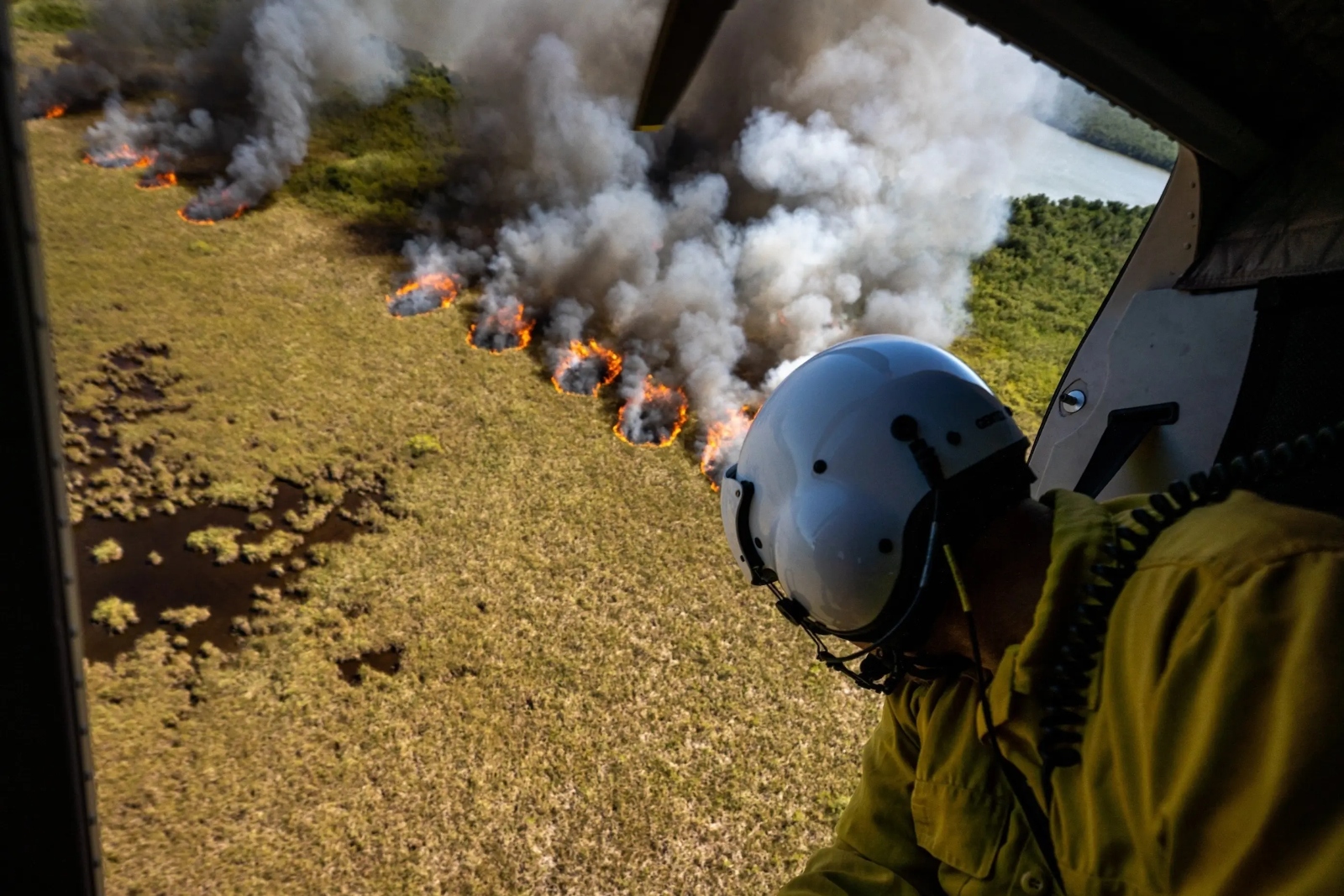 A wildland firefighter in a helicopter looks down on a fire in Everglades National Park