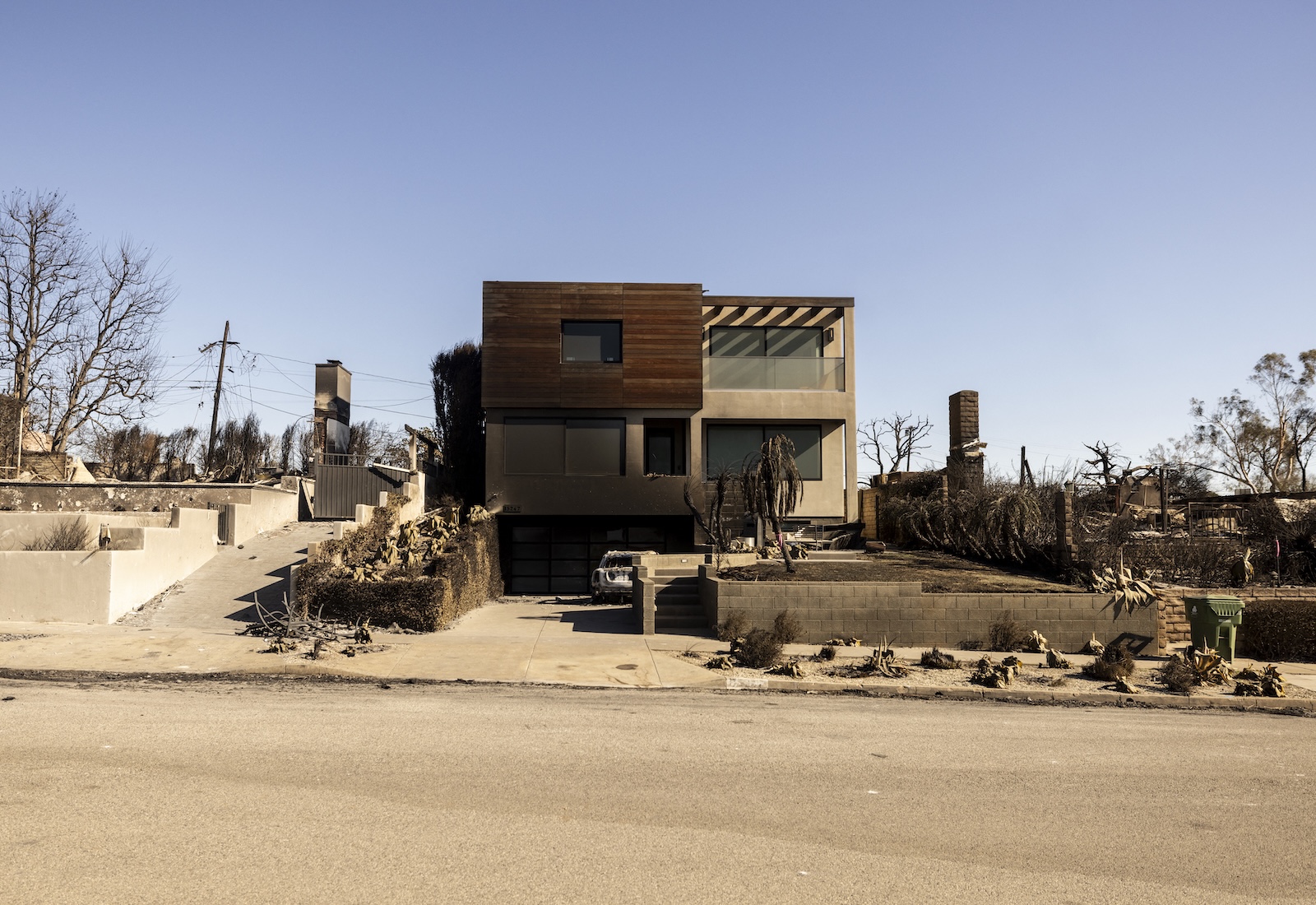 A rectangular house filmed from the street, while burning neighboring houses.