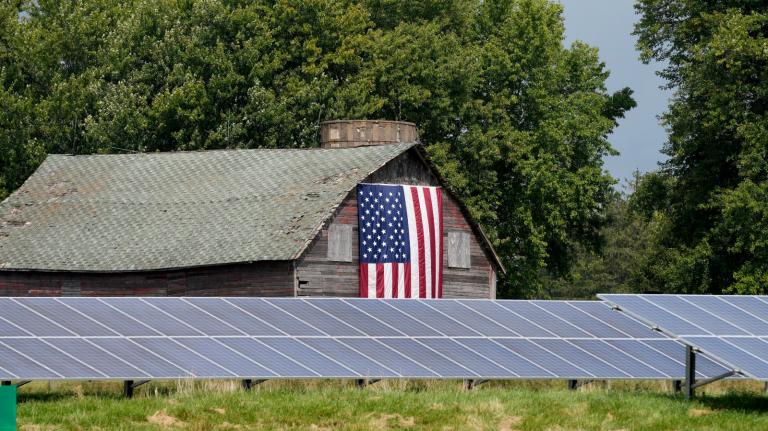 Photo of a barn with a flag behind a row of solar panels