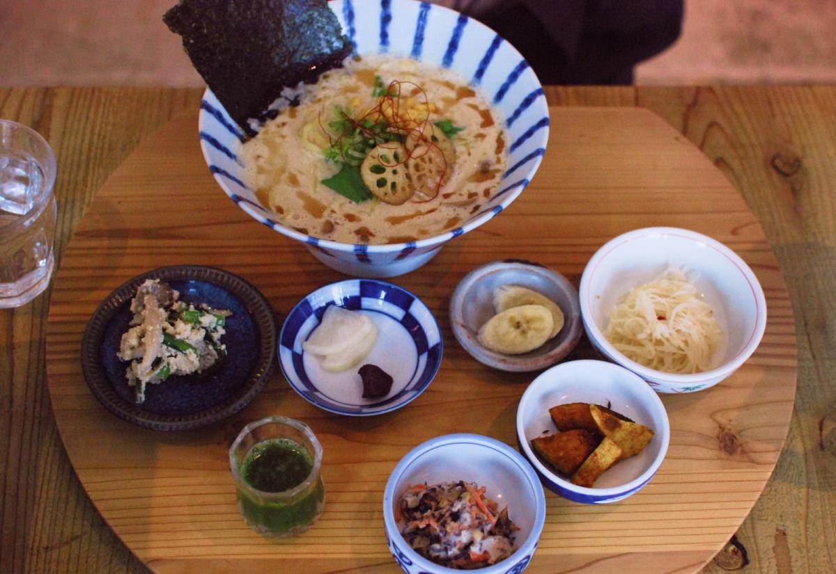 A bird's eye view of an inviting bowl of creamy ramen surrounded by small plates of vegetable garnishes