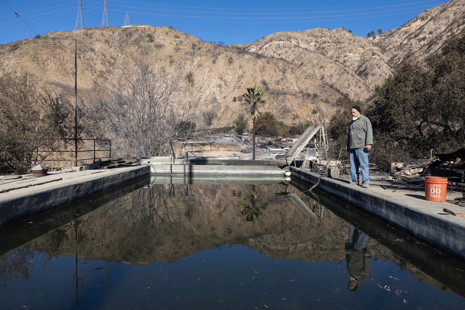 A man stands near a large pool with dry burned hills in the background