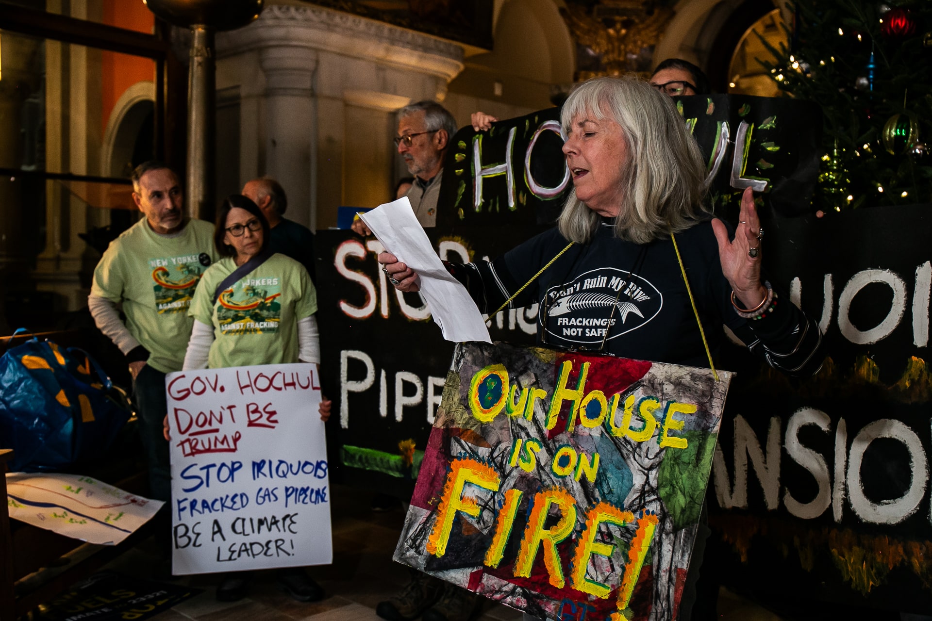 A group of protestors with signs stand while one woman reads from a sheet of paper