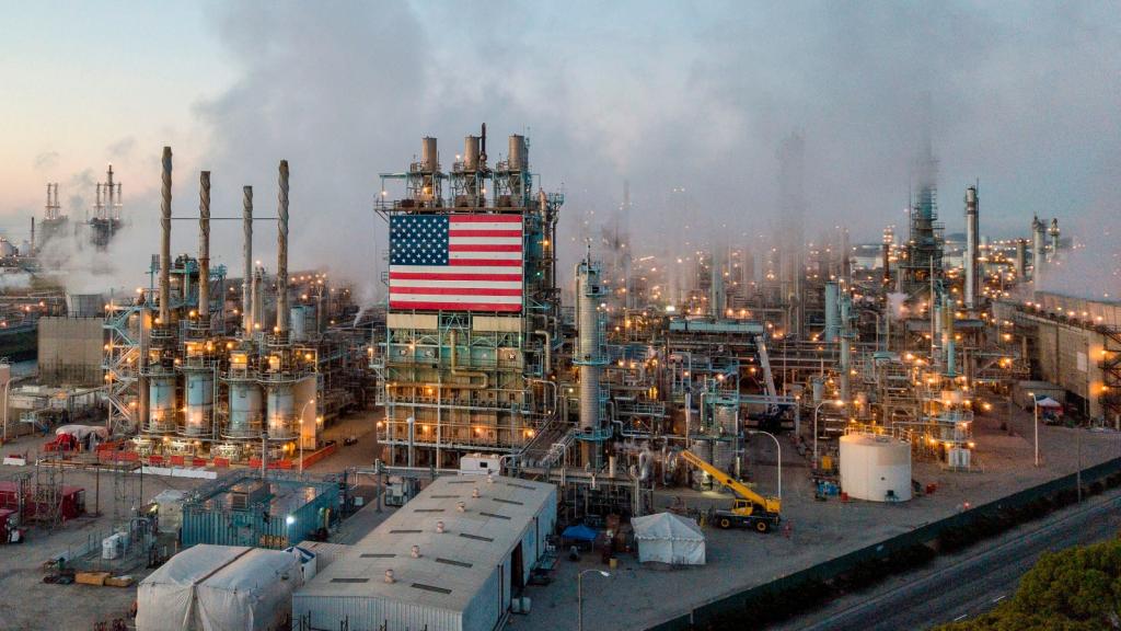 Smoke rising above an industrial complex decorated with an American flag