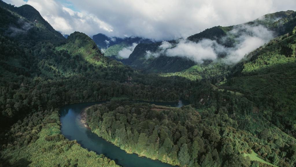 Aerial view of mountains and forests and river in Chile, with low-lying clouds