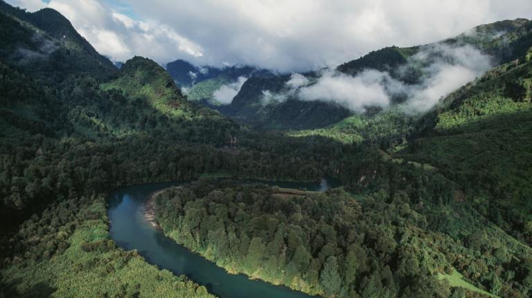 Aerial view of mountains and forests and river in Chile, with low-lying clouds