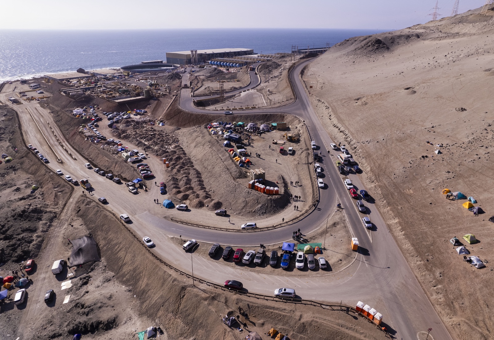 Aerial view of cars driving around a copper mine, with the ocean visible in the background