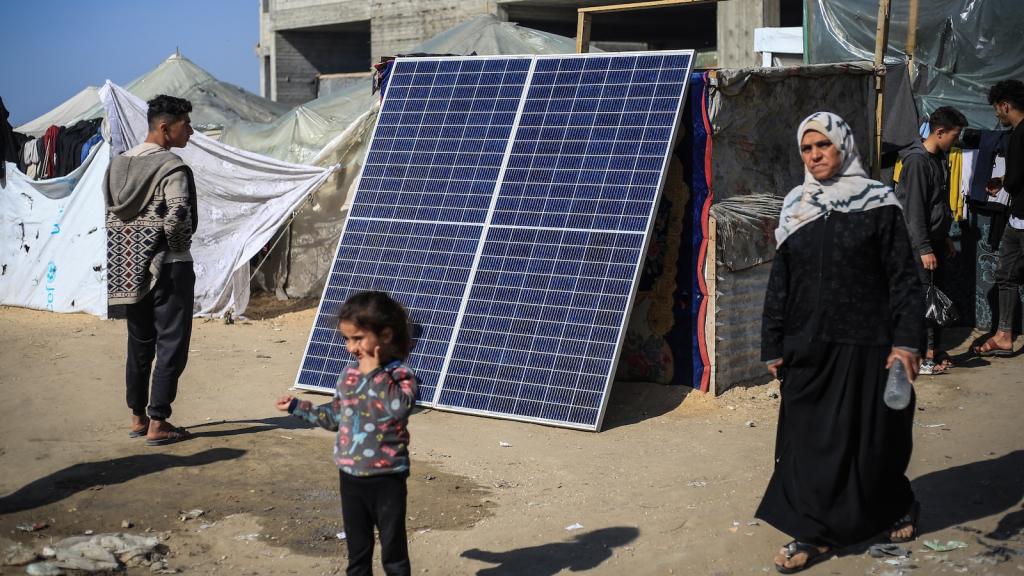 Palestinians walk by a solar panel, used by some to produce electricity in the refugee camps in Rafah.
