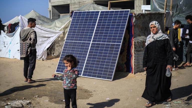 Palestinians walk by a solar panel, used by some to produce electricity in the refugee camps in Rafah.