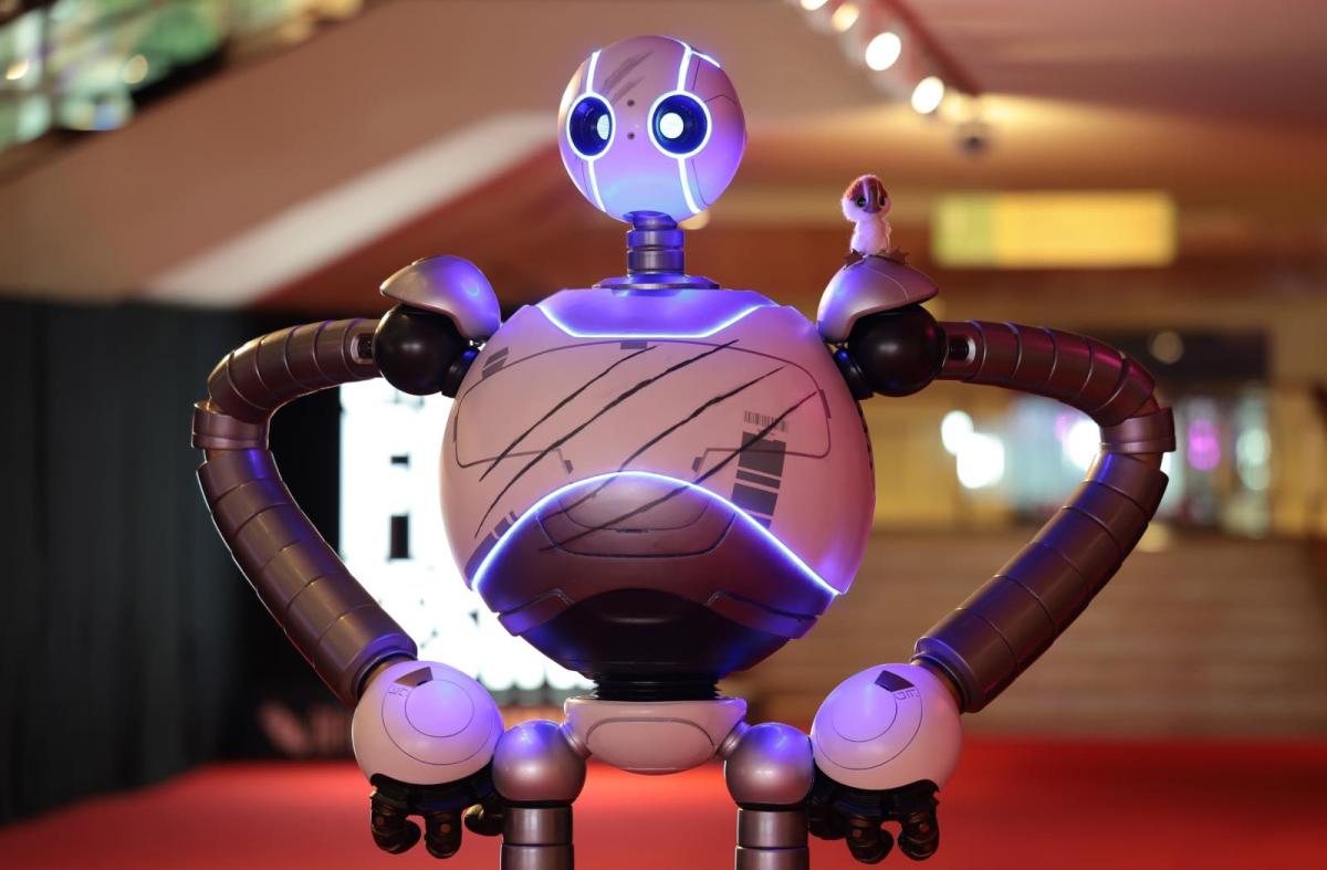 A photo of a shiny robot with a gosling on its shoulder, modeled after the animated character in The Wild Robot