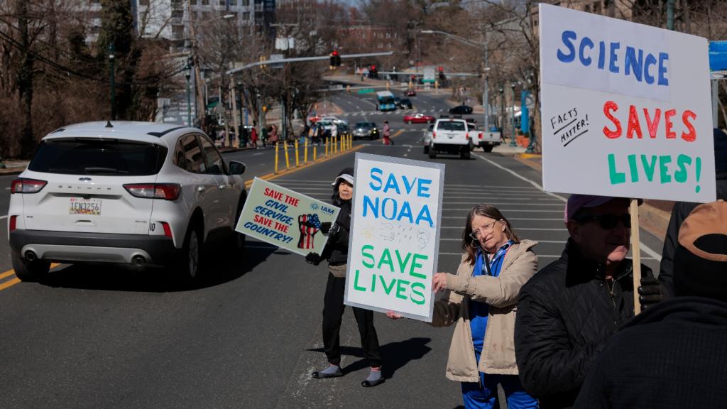 Women hold signs in the street that say Save Noaa and Science Saves Lives
