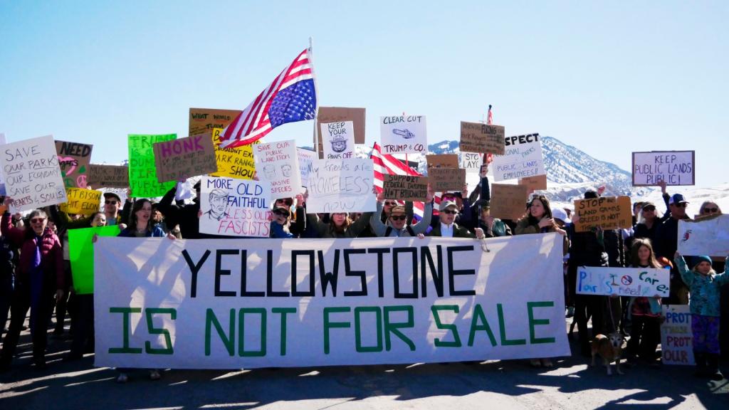A group of protestors in front of snowy mountains hold up a sign reading YELLOWSTONE IS NOT FOR SALE