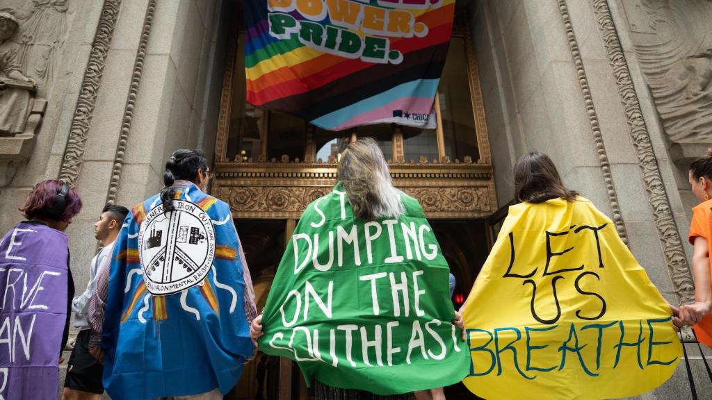 People stand in protest with backs to camera, wearing capes that have slogans painted on them.
