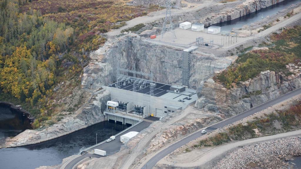 An aerial view of a grey building sitting in solid rock on a river