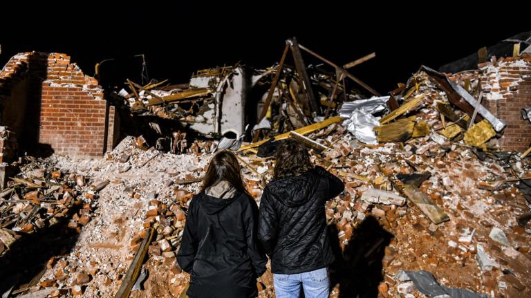 Photo of two people, facing away from the camera, surveying a damaged building