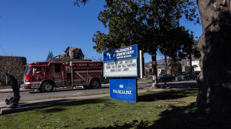 A sign that says Palisades Elementary School with a fire truck standing in the street next to it