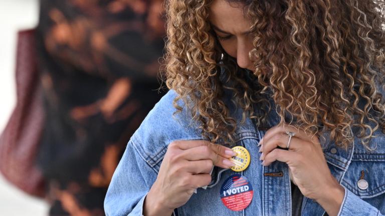 A young woman attaches a pin to her jacket after voting at a mobile outdoor vote center at SoFi Stadium in Los Angeles, California